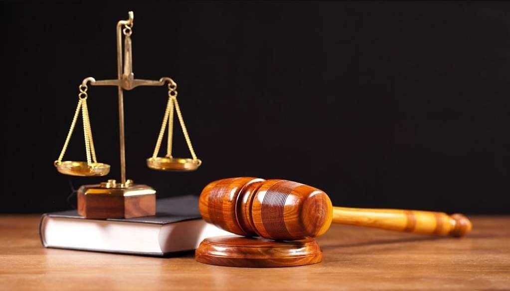 Gavel resting beside brass scales and a closed law book