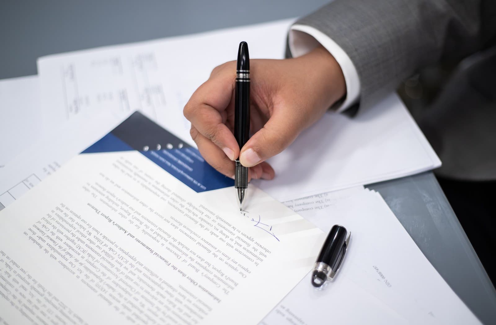 Hand signing a document with a fountain pen beside financial papers